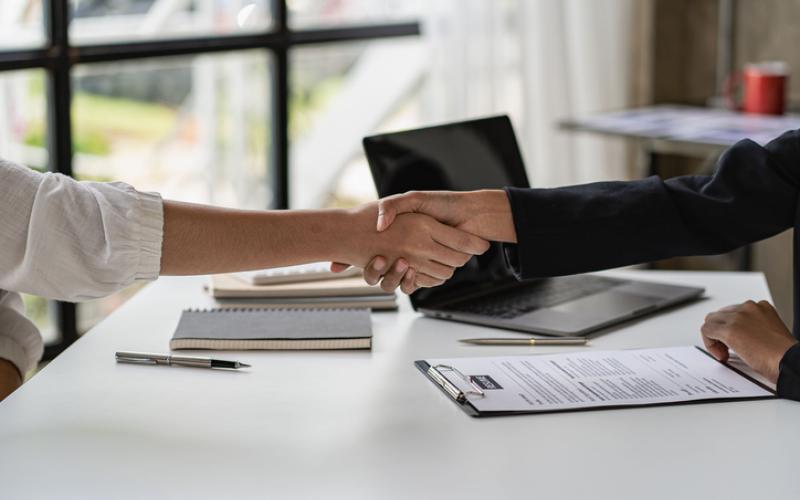 Photo of handshake between two female professionals over desk in front of window