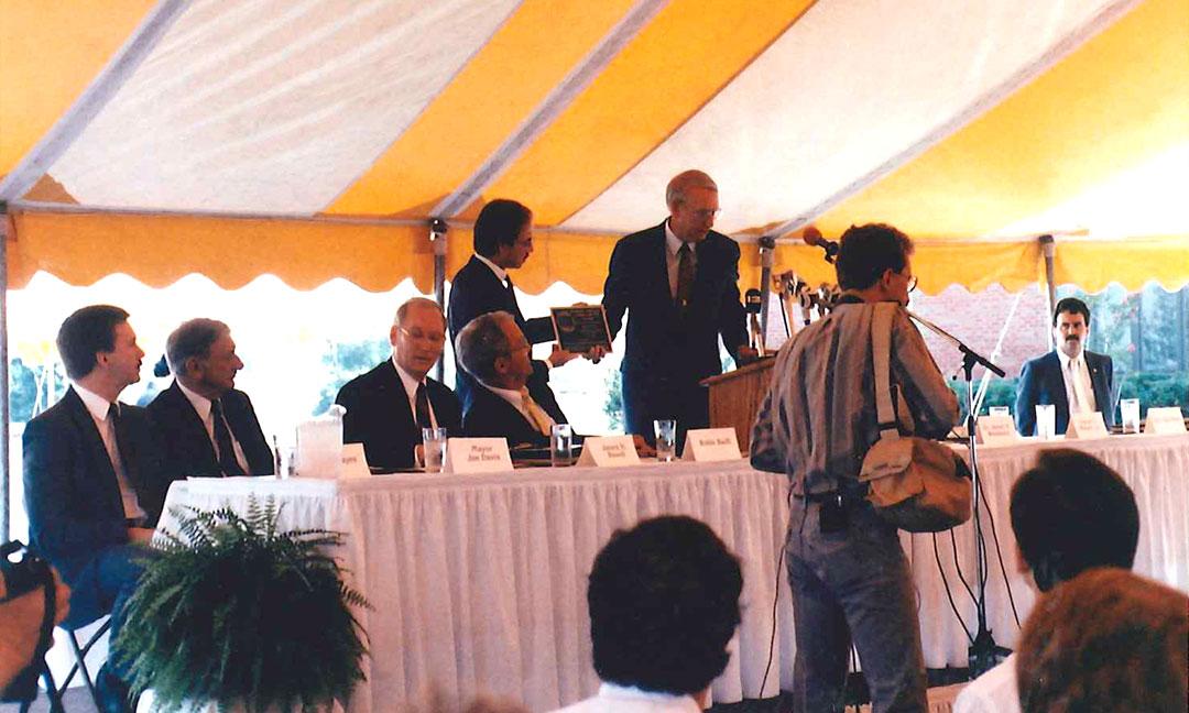 Governor Guy Hunt speaking and presenting plaque at podium outdoors under yellow and white tent pavillion at dedication of Alabama Supercomputer Center